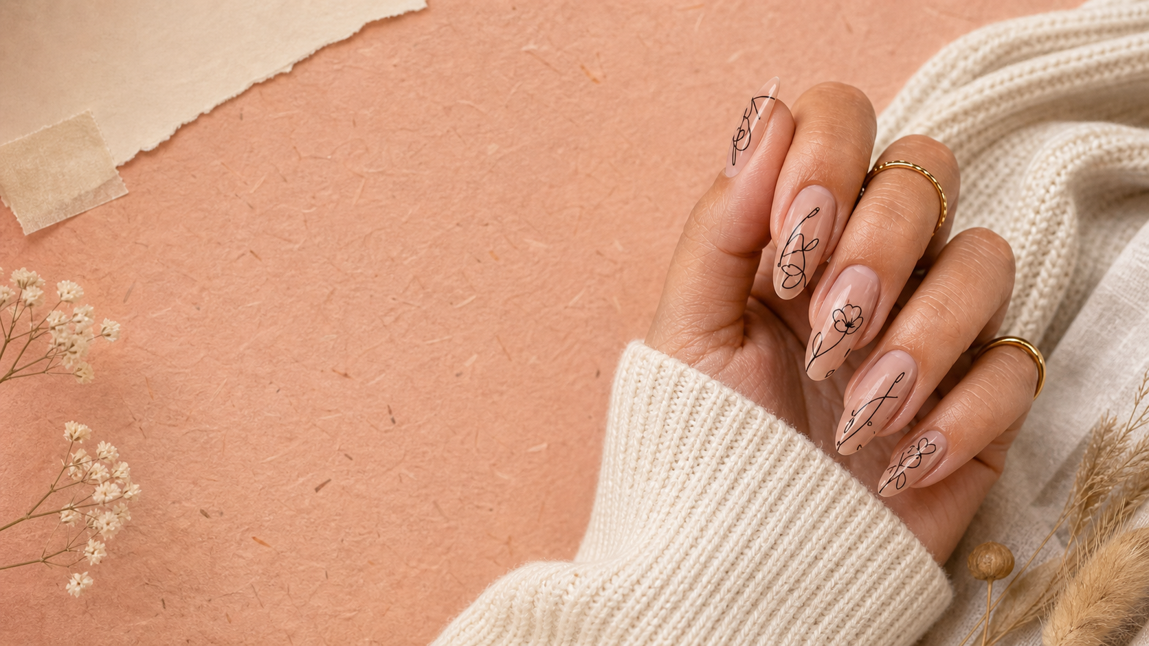 A hand with delicate fine-line nail art resting on blush paper
